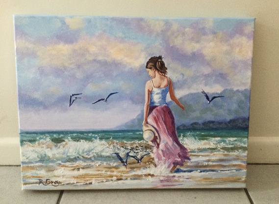 Woman in long dress walking on beach with seagulls flying nearby 