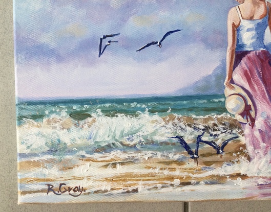 Woman in long dress walking on beach with seagulls flying nearby 