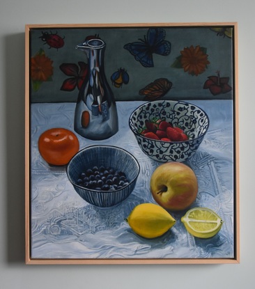 Bowls of berries, an apple, lemons, mandarin and silver oil jug on white tablecloth 
