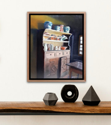 An old wooden kitchen cupboard in a corner beside a window that is bringing a ray of light casting shadows in the room.