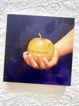 Youth's hand holding a gold apple inscribed with "for the most beautiful."