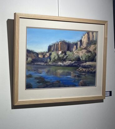 View over blue water, rocks in the foreground, and pale cliffs a short way behind in view.