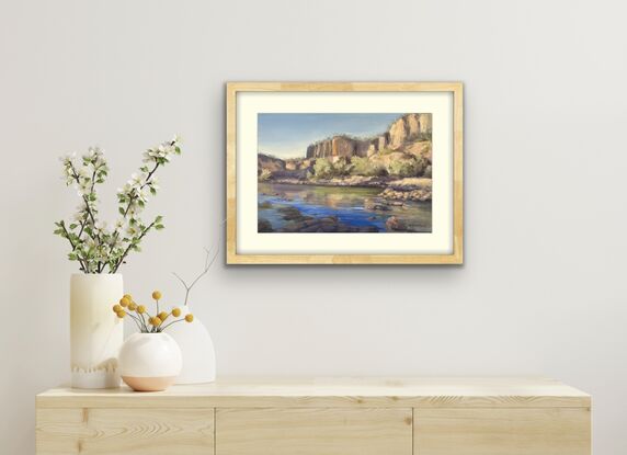 View over blue water, rocks in the foreground, and pale cliffs a short way behind in view.