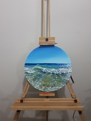 Turquoise and blue sea crashing into a wave on the shore of a beach. Oil paint on a round canvas.