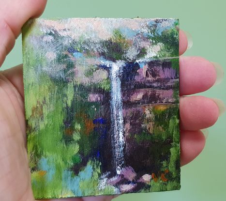 Miniature painting of a small waterfall viewed through a break in green forest; acrylic on stone tile by Victoria Collins.