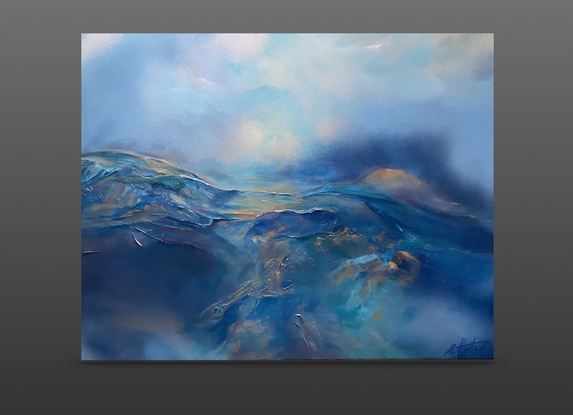 An atmospheric mountain and skies landscape painted in many shades of blue, highlighted in metallic soft gold and copper notes. It depicts the blue rolling mist over deep blue mountain ranges which meet the sky above