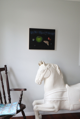 Painting of black night sky with band of the milky way in the upper third of the painting. In the foreground are cat eye marbles, a green granny smith apple, fairy bread with a bite taken out of it, a strawberry cut in half and another whole strawberry.