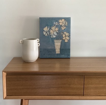 A still life of geometric cream coloured flowers, sitting in a decorative vase, blue background.