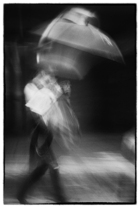 Fighting the Wind. 
"I didn’t invent the rainy day, I just own the best umbrella." From the ‘Ordinary Interesting - Street Streak’ body of work. A single shot in-camera by emerging artist Ann Parrott with a Limited Edition of 21. Brisbane city.