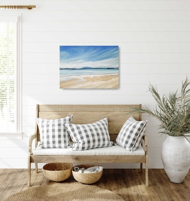 Wispy white clouds in the bright blue sky, mountainous horizon, calm blue waters, patterns in the sand.