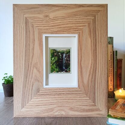 Miniature painting of a small waterfall viewed through a break in green forest; acrylic on stone tile by Victoria Collins.