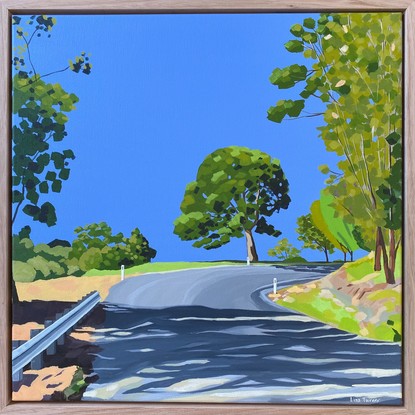 Shadowed road leading up a hill and around the bend with tree in background under perfect clear blue skies.