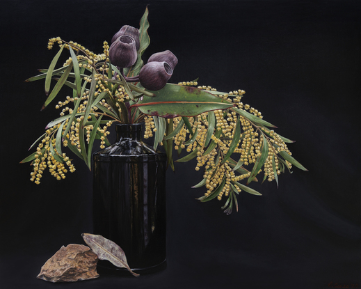 Still life of black, Hendrick’s Gin bottle filled with golden wattle and gumnut bunches on a black background. Warm-coloured, angular rock and one dried leaf perched in front of the bottle. Framed in Japan black stained frame.