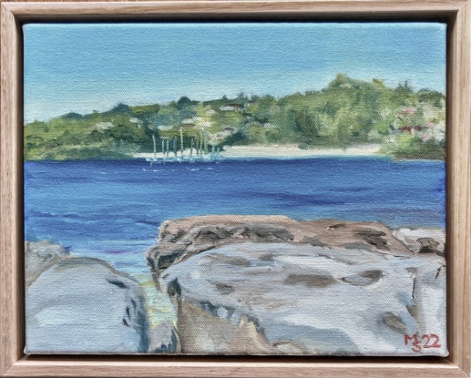 View across an exoanse of water to a small beach with boat moorings - rocks in foreground