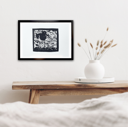 Lino Cut portrait of an Australian Pied Oystercatcher Bird standing on rocks with a background of swirling water. The bird has a very long beak. It’s feathers are black with a white breast and belly. 