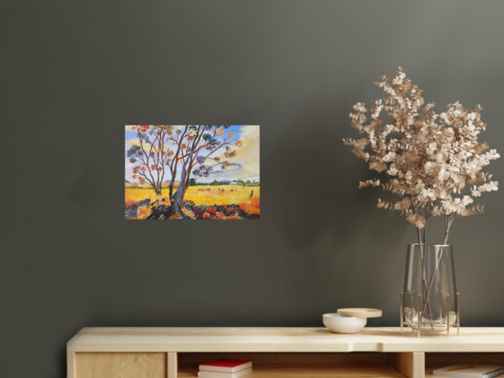 a field of gold under a blue and cream sky with distant blue ranges and a farm with a herd of cows grazing and a couple of gum trees with quirky foreground colours