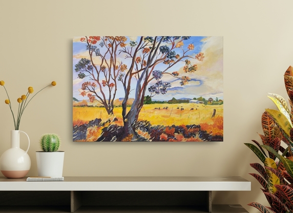 a field of gold under a blue and cream sky with distant blue ranges and a farm with a herd of cows grazing and a couple of gum trees with quirky foreground colours