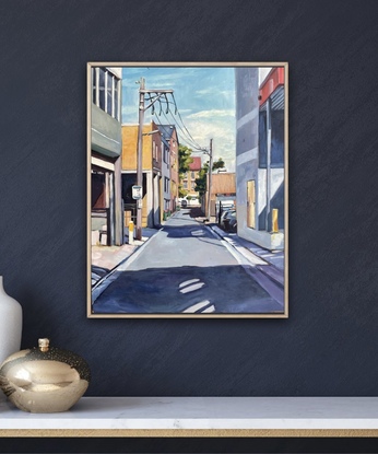 an urban back lane showing the buildings and their shadows on either side, with a public school in the distance. Framed in oak