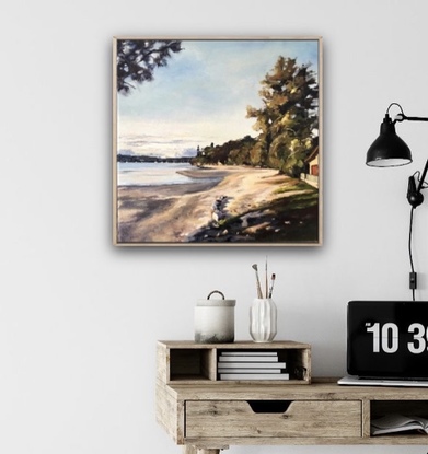 A beach scene of a bay at sunset as last light results in  golden light and long shadows. There are trees along side the sand with sunlight hitting the trees. Headland and boats in the the distance.  