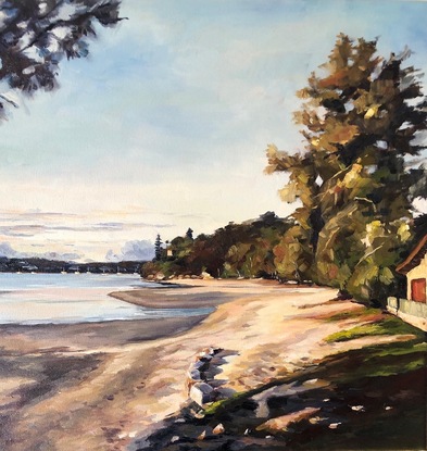 A beach scene of a bay at sunset as last light results in  golden light and long shadows. There are trees along side the sand with sunlight hitting the trees. Headland and boats in the the distance.  