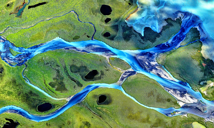 Aerial view of blue glacial waters criss-crossing the green Arctic landscape of Lapland in northern Sweden that form interconnected abstract patterns.