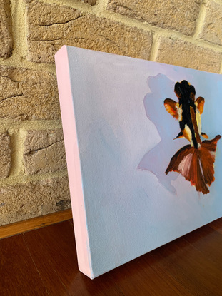 Floating Fish features an orange, yellow, black and white goldfish floating across a sky blue surface casting a shadow. It’s painted with oil paint. The background is painted flat while the goldfish pops out with textured brushstrokes. It is landscape orientation. The sides are 4 cm deep and are painted dusty pink.

Original artwork by Rebecca Hepworth.