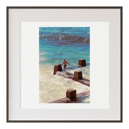 A man balancing and almost slipping on an ocean pool barrier 