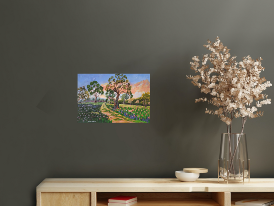 
Riverina Bushwalk is a delightful natural serene landscape painting, featuring a path leading into the distance, with colourful flowers in both cool and warm shades, Australian gum trees scattered around the landscape under a lively warm coral and blue sky.