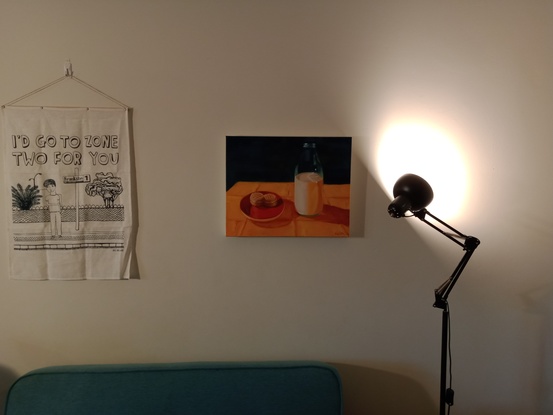 Two melting moments sit side by side in a red saucer. Next to this on the right there is a glass bottle of milk, 3/4 full. These are both sitting on a bright yellow tablecloth. The background is a dark bluel