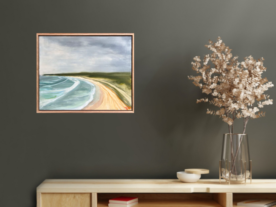 An elevated view of surf, sand, and green headland under a stormy sky