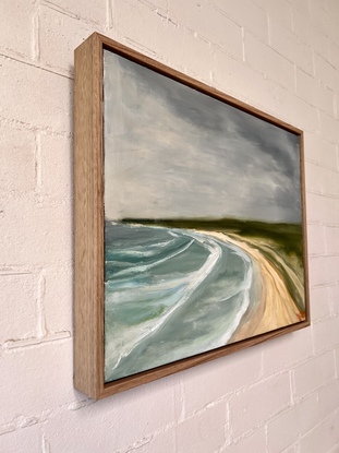 An elevated view of surf, sand, and green headland under a stormy sky