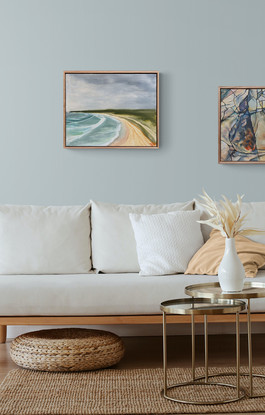 An elevated view of surf, sand, and green headland under a stormy sky