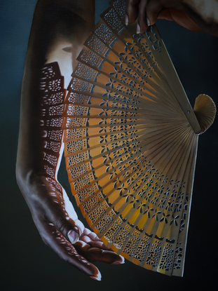 Hand holding an intricate fan with light streaming through the fan, casting a pattern of shadows across the hand.