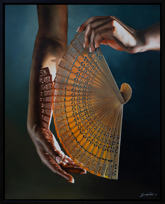 Hand holding an intricate fan with light streaming through the fan, casting a pattern of shadows across the hand.