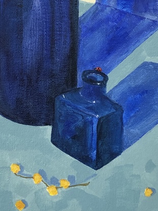 Branches of yellow wattle in a blue and white vase, with blue glass bottles and a pile of books.