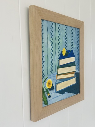 Pile of books on a striped blue tablecloth, with dandelions and vine wallpaper behind. 