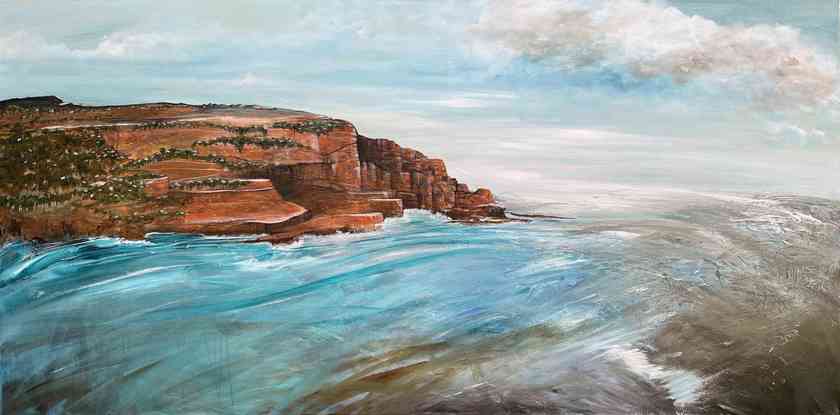 Blue and white fluffy clouds overlooking turbulent blue and white waters and tan rocky cliff.
