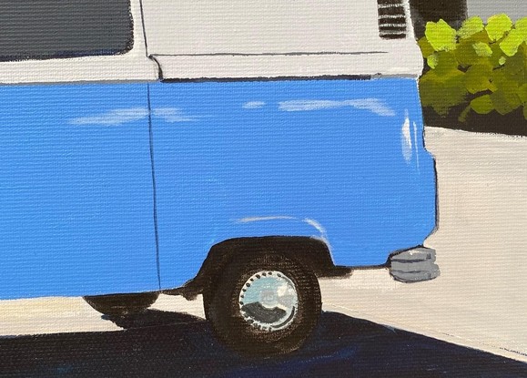 Blue Kombi van in carpark near large trees, both casting strong shadows in the foreground with hint of ocean in the background under and clear blue sky. 