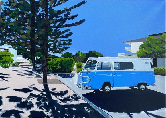 Blue Kombi van in carpark near large trees, both casting strong shadows in the foreground with hint of ocean in the background under and clear blue sky. 