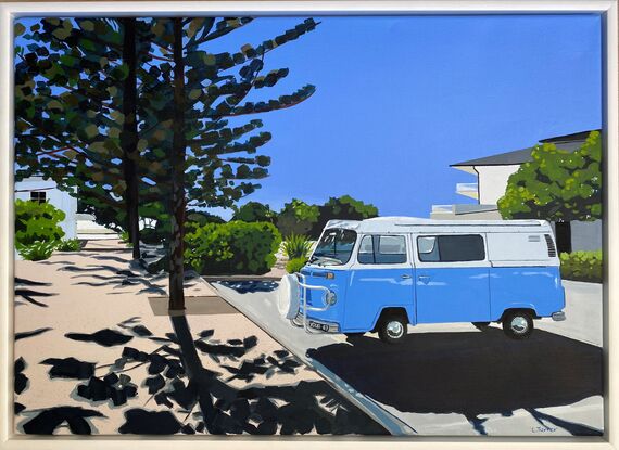 Blue Kombi van in carpark near large trees, both casting strong shadows in the foreground with hint of ocean in the background under and clear blue sky. 