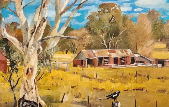 A scenic view of rural outback Australia. Includes a large white gum tree in the foreground with old sheds under a bright blue cloudy sky.