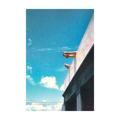 An angled view of a concrete wall and two pairs of feet propped up hanging over against a bright blue sky.