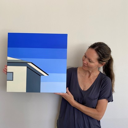 Simple cream/beige coloured house facing bright sun with side wall in shadow before striped, geometric blue sky.