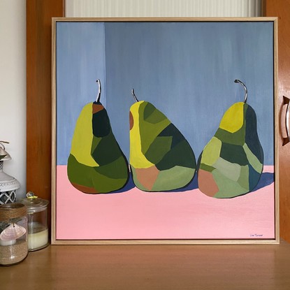 3 green pears in triangle formation on a pink surface before a grey wall.