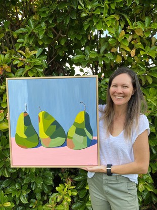 3 green pears in triangle formation on a pink surface before a grey wall.