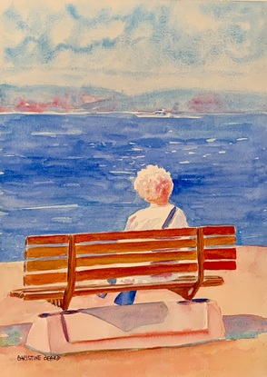 Women sits on a bench by the beach in the sunshine.