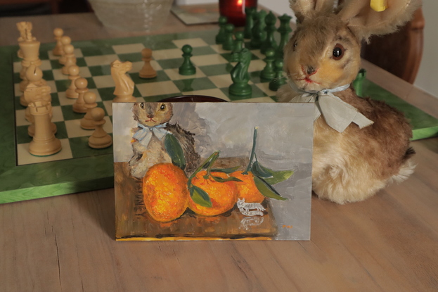 Impressionistic painting of a grey bunny on a Fry's Homeopathic Cocoa wooden box. In front of them sits 3 beautiful mandarin oranges, with stems and leaves, and a silver medieval replica pin  which is of a cat with a mouse in its mouth, it reads "vi sis mis" - I have the mouse.