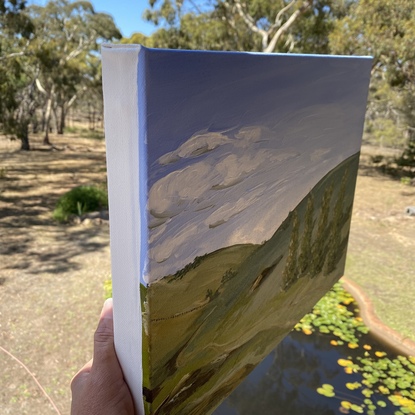 This country landscape depicts olling green hills and a row of trees, a winding dirt track and rocky outcrops under a hazy blue sky. 