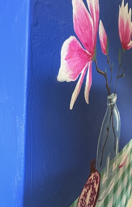 A still life depicting - a glass vase with two magnolia flowers and buds, a pomegranate leaning against the vase and a single fallen petal sitting nestled into the gingham creased table cloth. With a bold pacific blue backdrop 