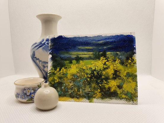 Miniature landscape of dark blue fields and hills with yellow wattle bushes, by Australian artist Victoria Collins